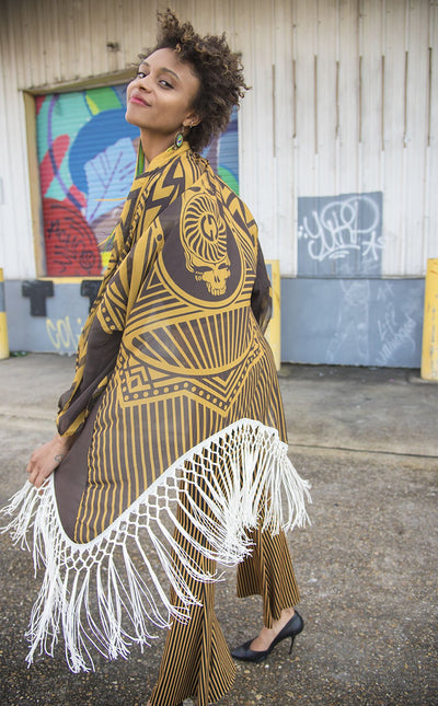 Kimono with long braided cream fringe. The artwork is of a Stealie with stripes based off the 1977 album cover. It is the gold and brown colors mimicking the original album cover. The model is African American and smiling. 