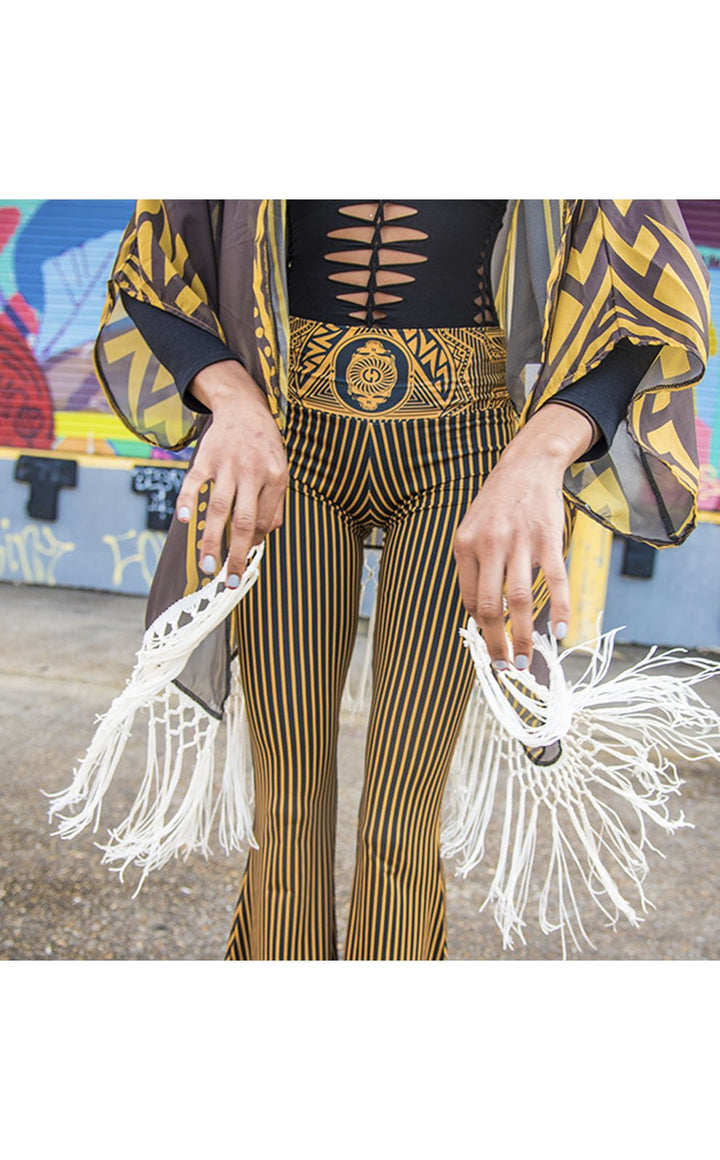 Kimono with long braided cream fringe. The artwork is of a Stealie with stripes based off the 1977 album cover. It is the gold and brown colors mimicking the original album cover. This is a close up shot of the models torso with the fringe in motion