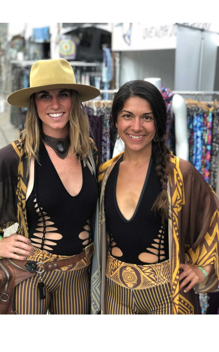 Kimono with long braided cream fringe. The artwork is of a Stealie with stripes based off the 1977 album cover. It is the gold and brown colors mimicking the original album cover. There are two models both facing forward smiling.  You can only see the top of the kimono not the bottom or the fringe.