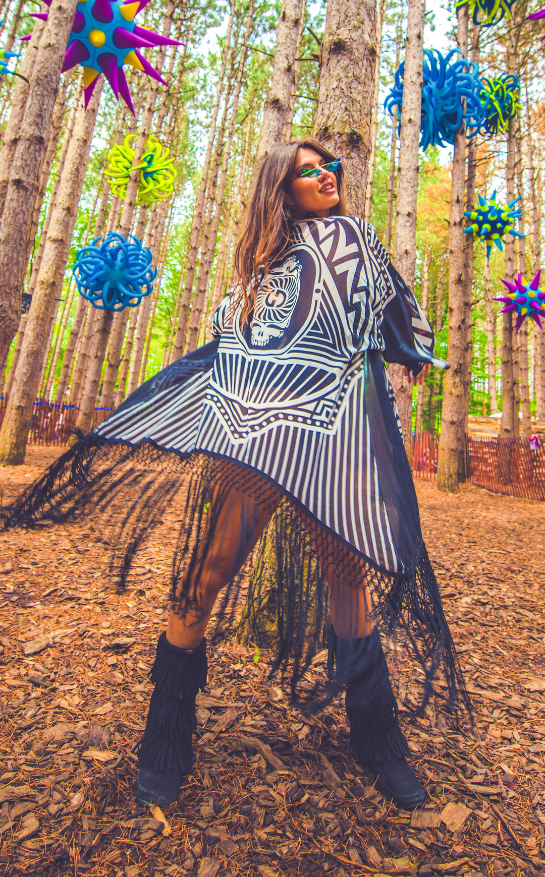 Kimono with long braided black fringe. The artwork is of a Stealie with stripes based off the 1977 album cover. It is the black and white. The model facing forwards with the kimono in motion swirling around her.  This image really shows how much the fringe can move in motion.  