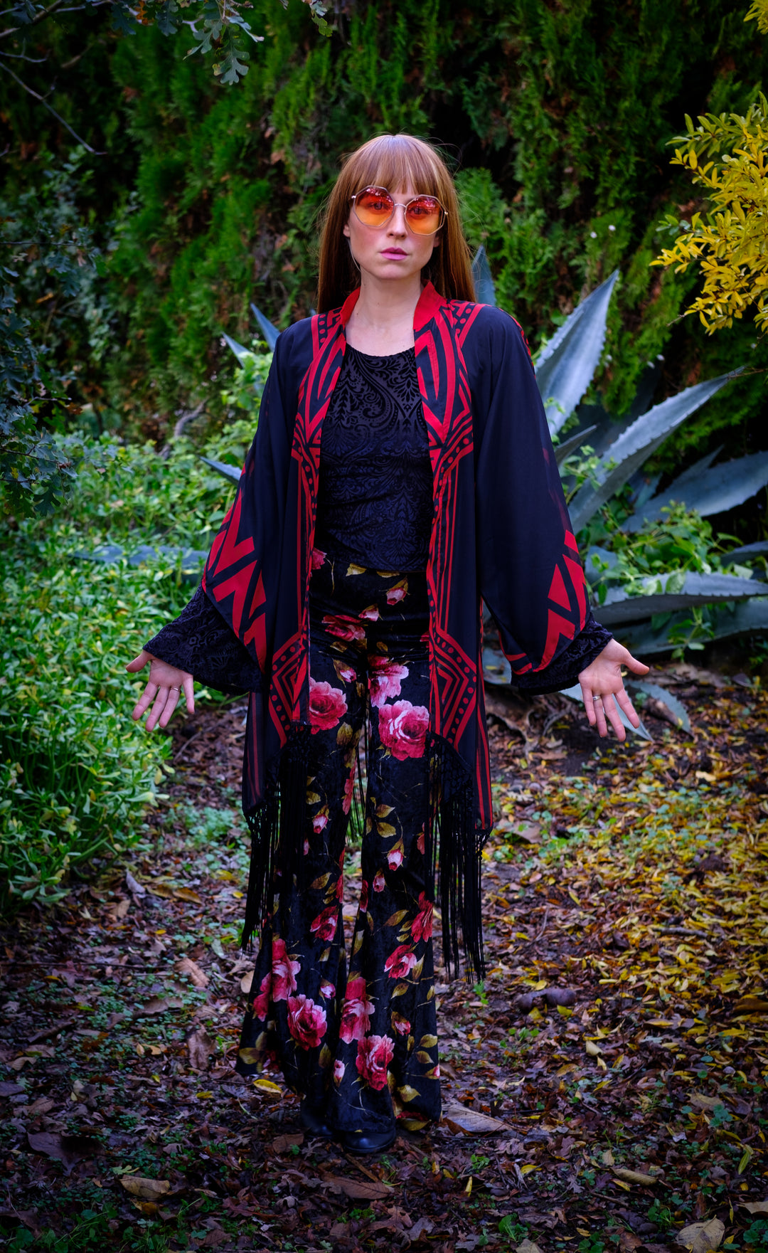 Kimono with long braided black fringe. The artwork is of a Stealie with stripes based off the 1977 album cover.  The print is black and red. The model is faced forward wearing large sunglasses that have an orange tint to them.  